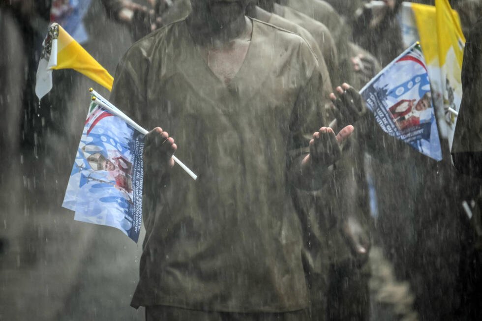 Des détenus brandissent des drapeaux portant des images commémorant la visite du pape Léon XIV, alors qu'ils prient sous la pluie lors de sa visite à la prison de Bata, en Guinée équatoriale, le 22 avril 2026, au dixième jour d'un voyage apostolique de 11 jours en Afrique.