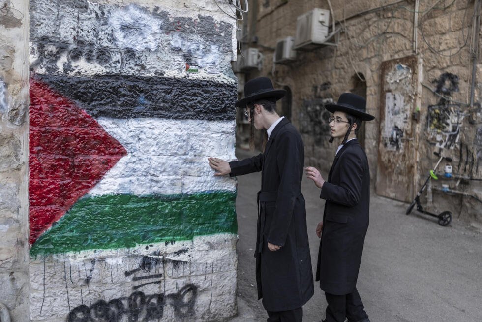 Des membres de Neturei Karta, une organisation de juifs ultra-orthodoxes antisionistes, se tiennent à côté d'une fresque représentant le drapeau palestinien lors d'une manifestation contre l'État d'Israël, dans le quartier de Méa Shéarim, à Jérusalem, le 22 avril 2026, alors qu'Israël célèbre son 78e Jour de l'indépendance.