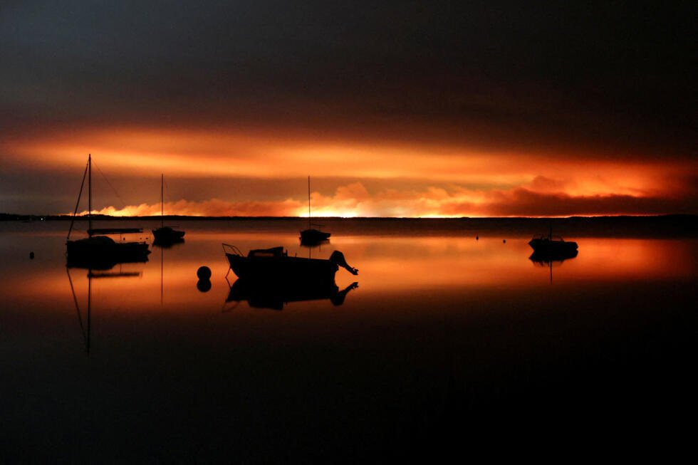 En images : près du bassin d'Arcachon, le feu s'attaque à nouveau à la forêt des Landes 4 Des bateaux à Lacanau avec un feu de forêt virulent en arrière-plan, le 23 juillet 2026.